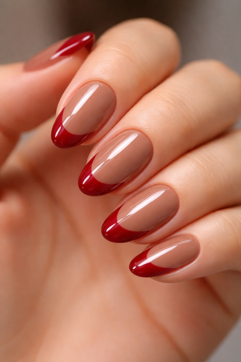 Nail with cherry red curved tip over nude brown base.