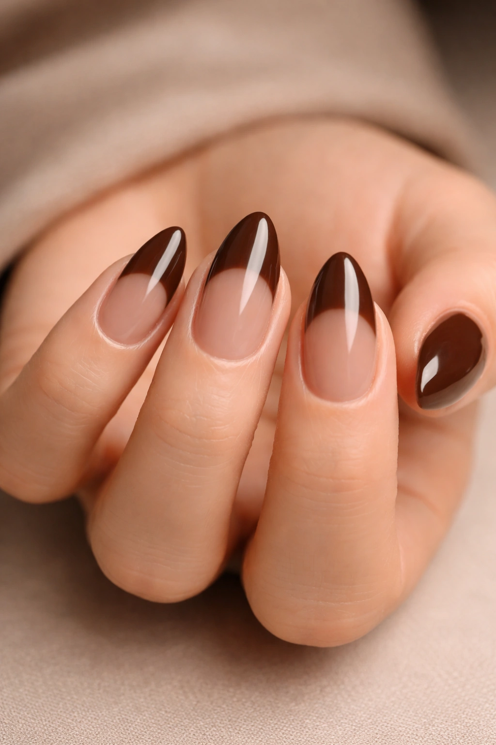 Close-up of chocolate brown almond nails with glossy finish on a neutral background