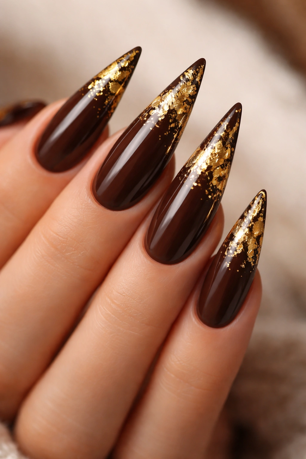 Close-up of chocolate brown stiletto nails with gold foil accents