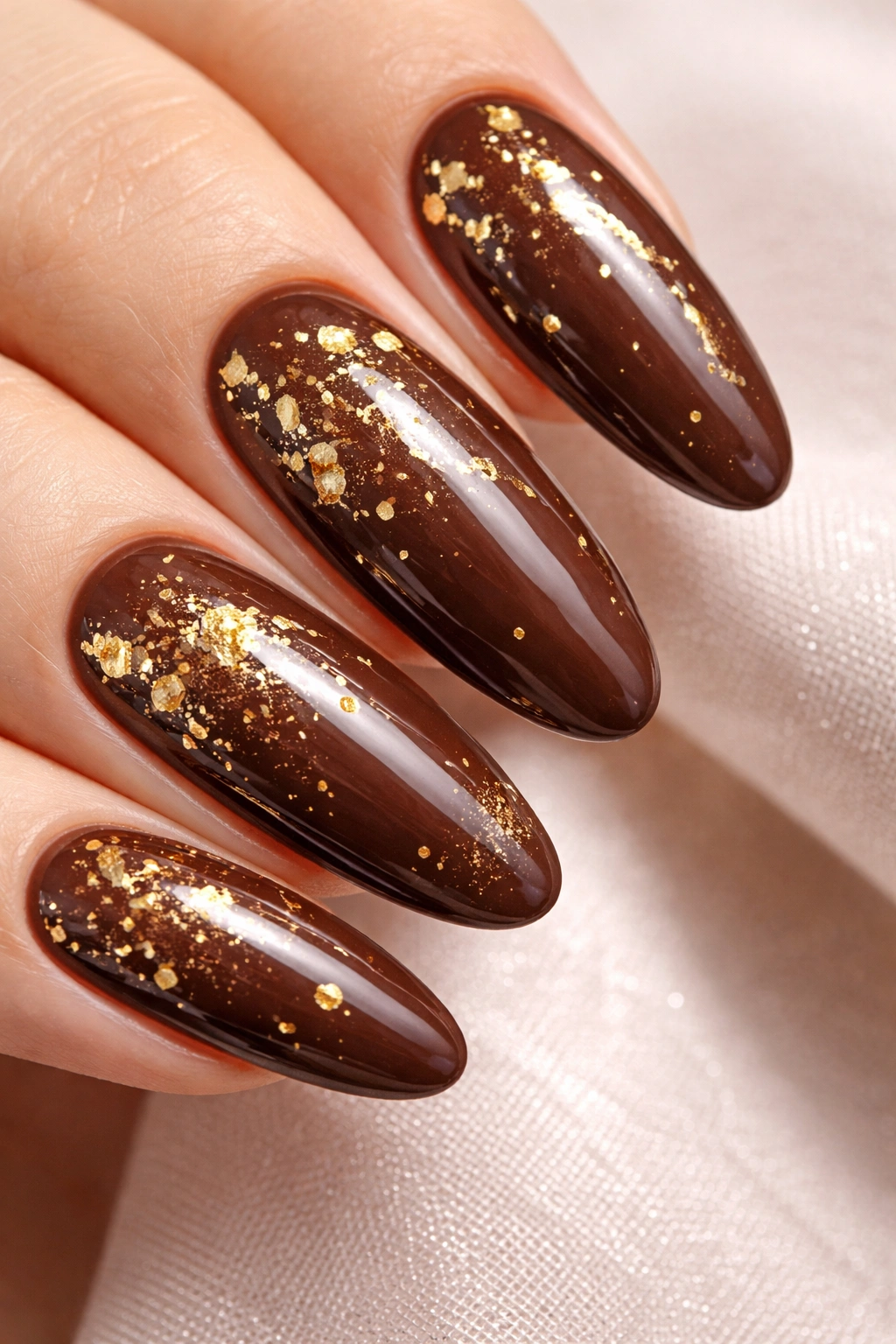 Close-up of chocolate brown long oval nails with gold flakes