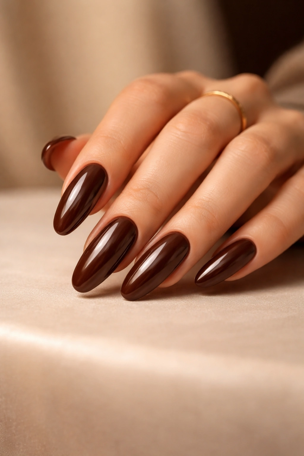 Close-up of a hand with long round chocolate brown nails on a neutral surface