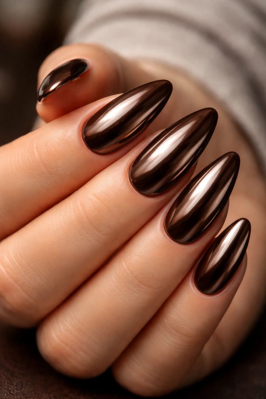 Close-up chocolate chrome almond nails with reflective brown finish