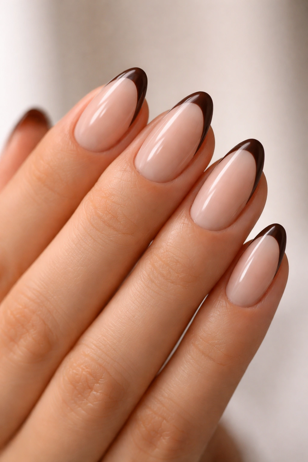 Close-up of short almond nails with a sheer nude base and chocolate French tips