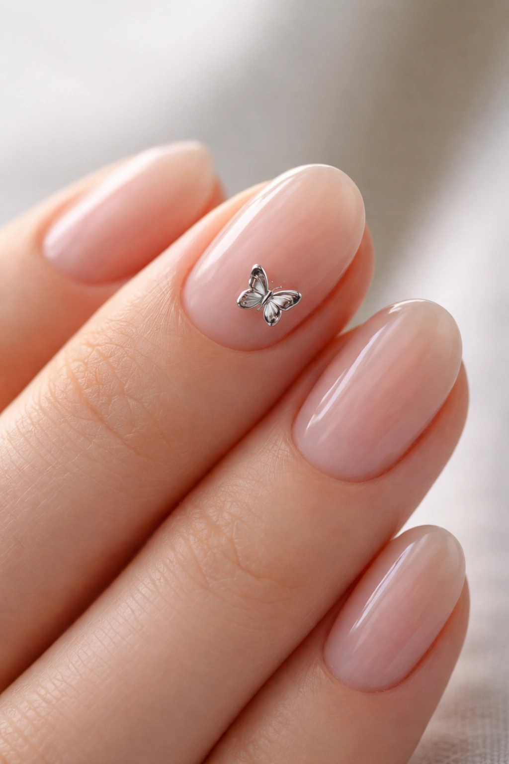 Close-up of a chrome butterfly charm on a short oval nail with a sheer base.