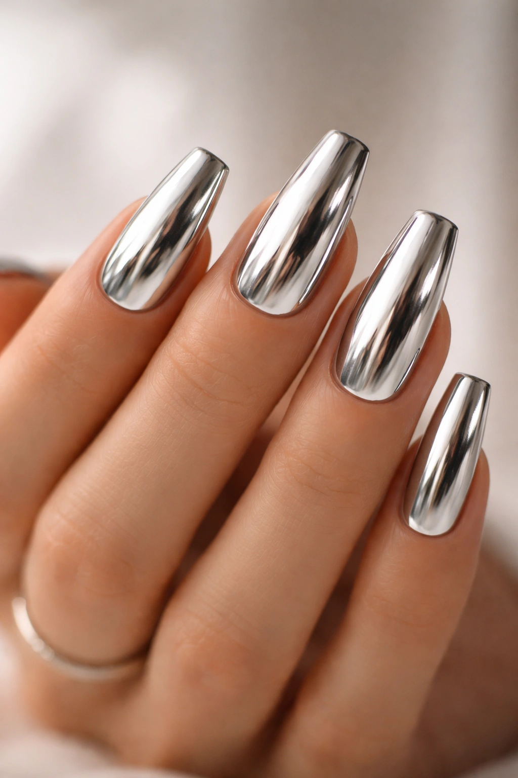 Close-up of medium-length coffin nails with chrome mirror finish on a neutral background