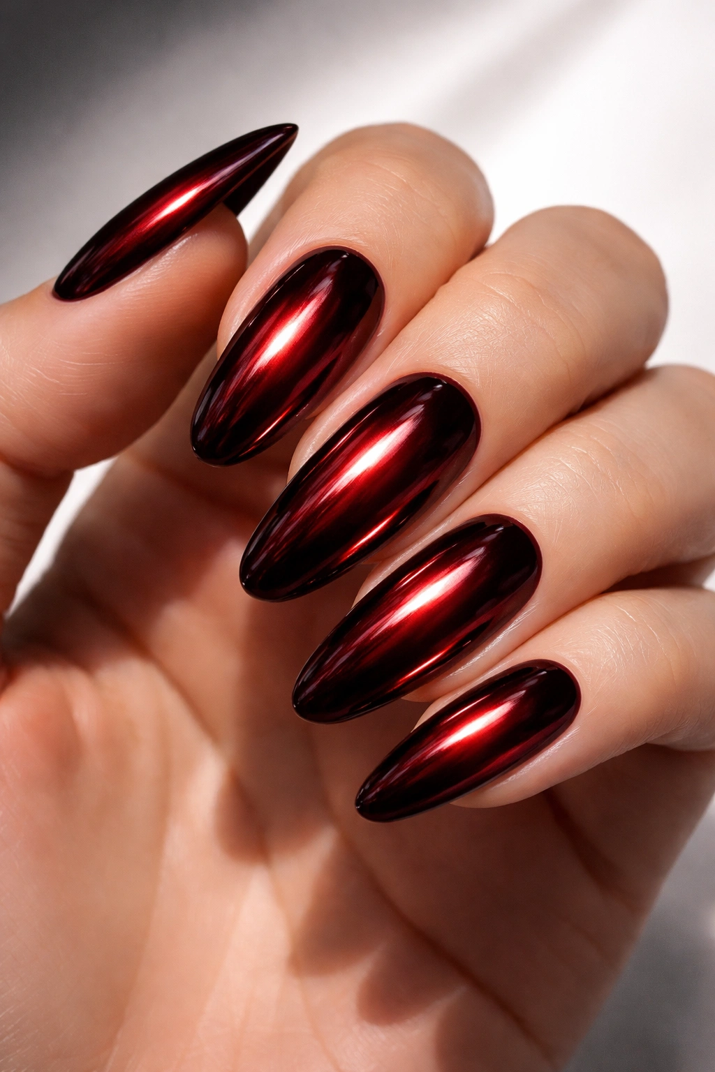 Close-up of chrome-dark red nails with mirror-like metallic finish on a hand