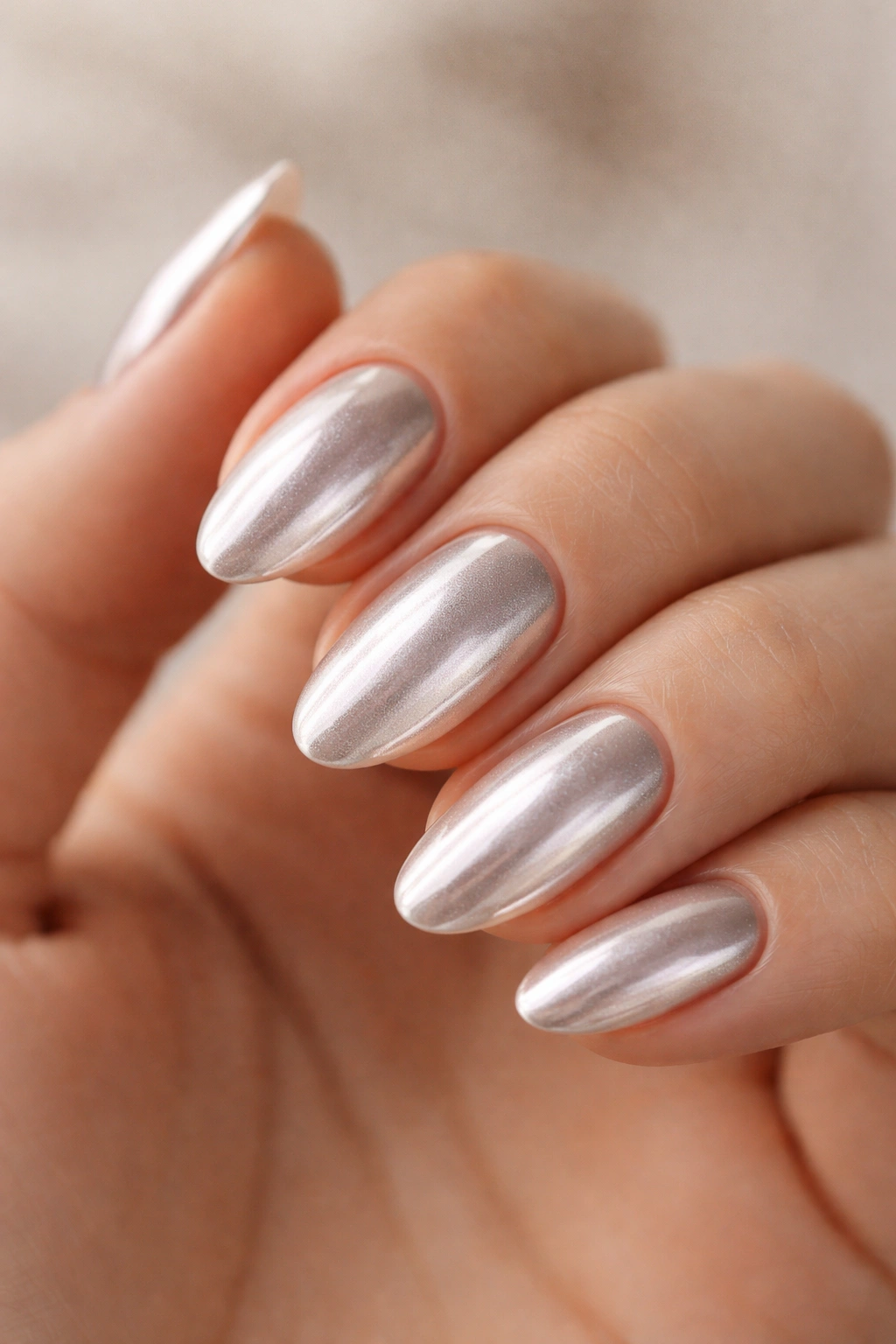 Close-up of short almond polygel nails with chrome dust finish in silver tones