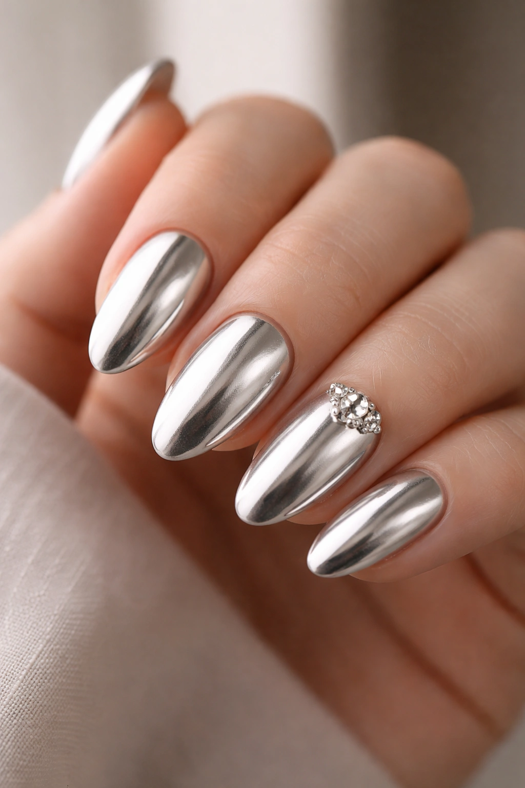 Close-up of chrome almond nails with a crystal cluster on the accent nail