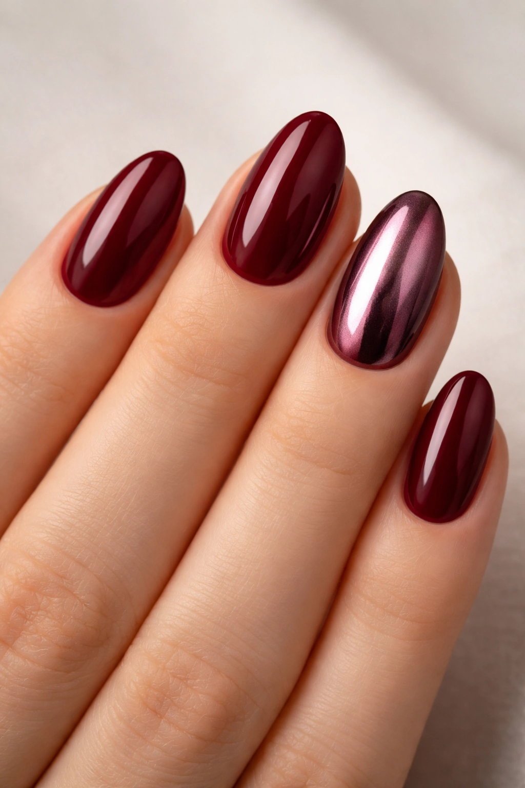 Close-up of maroon almond nails with a single chrome accent nail