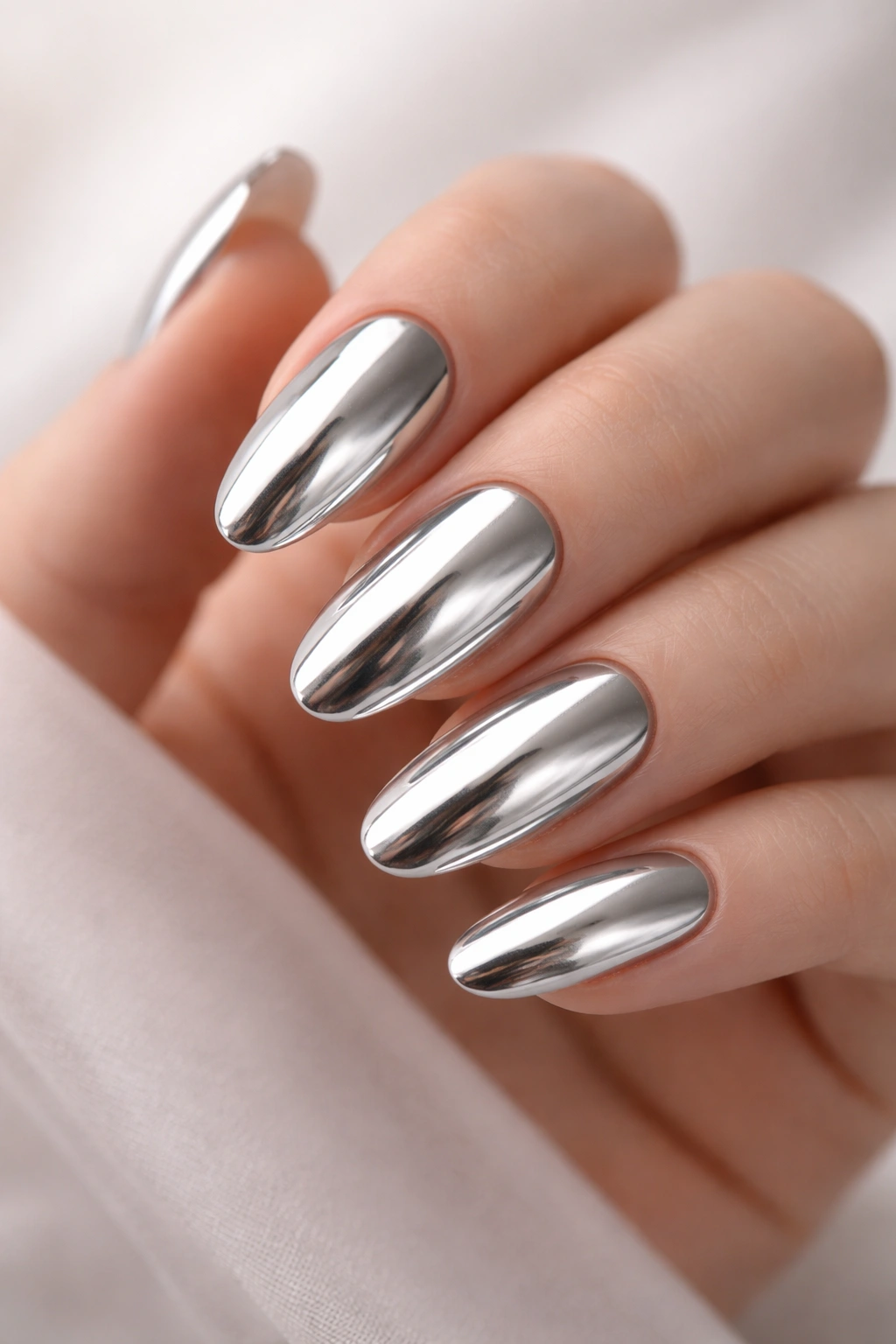 Close-up of long oval nails with chrome mirror finish reflecting light.
