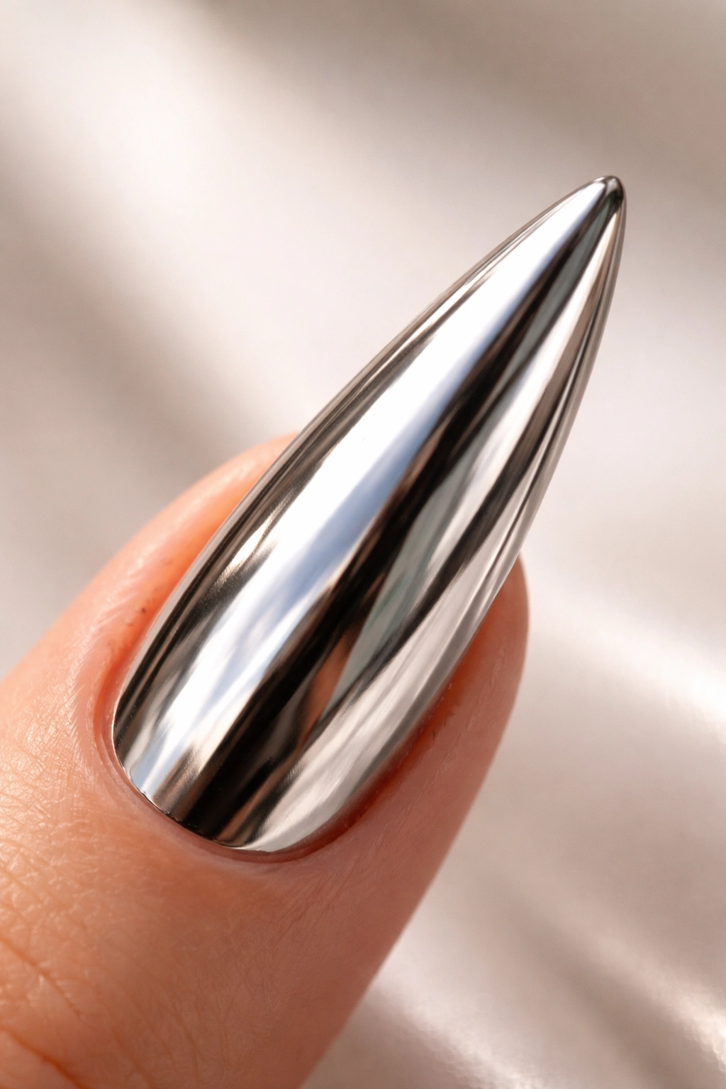 Close-up of chrome mirror finish stiletto nail on neutral background