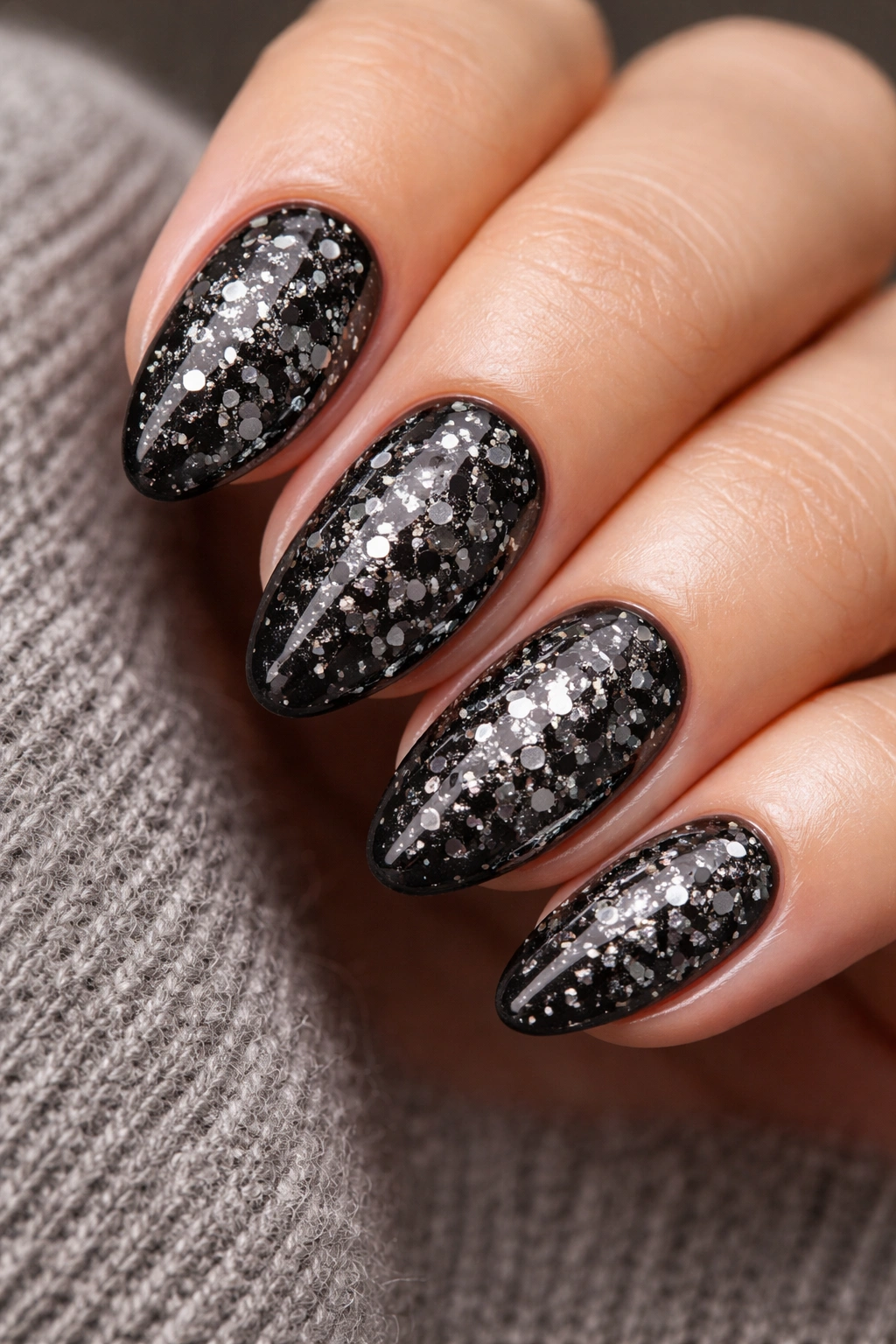 Close-up of short almond nails with chunky black glitter on a black base