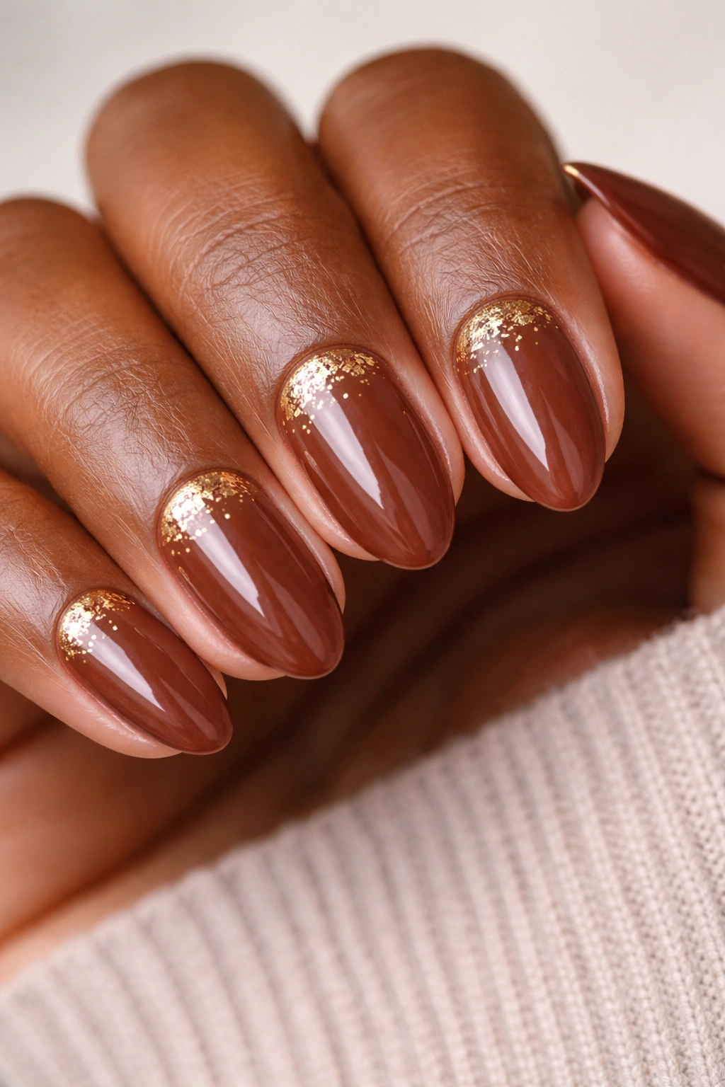 Close-up of cinnamon brown almond nails with gold foil accents