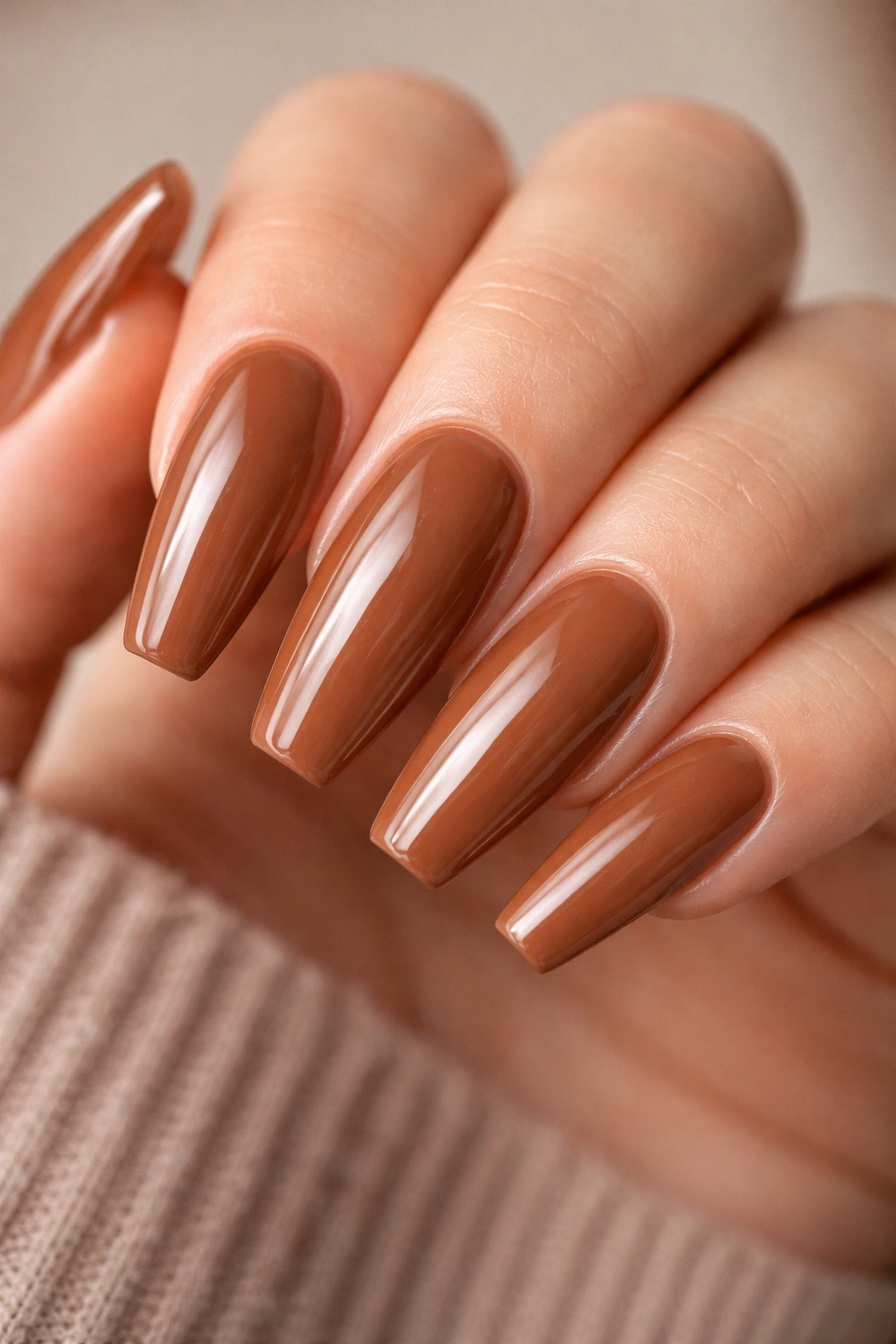 Close-up of cinnamon latte brown ballerina nails with a glossy finish on a neutral background