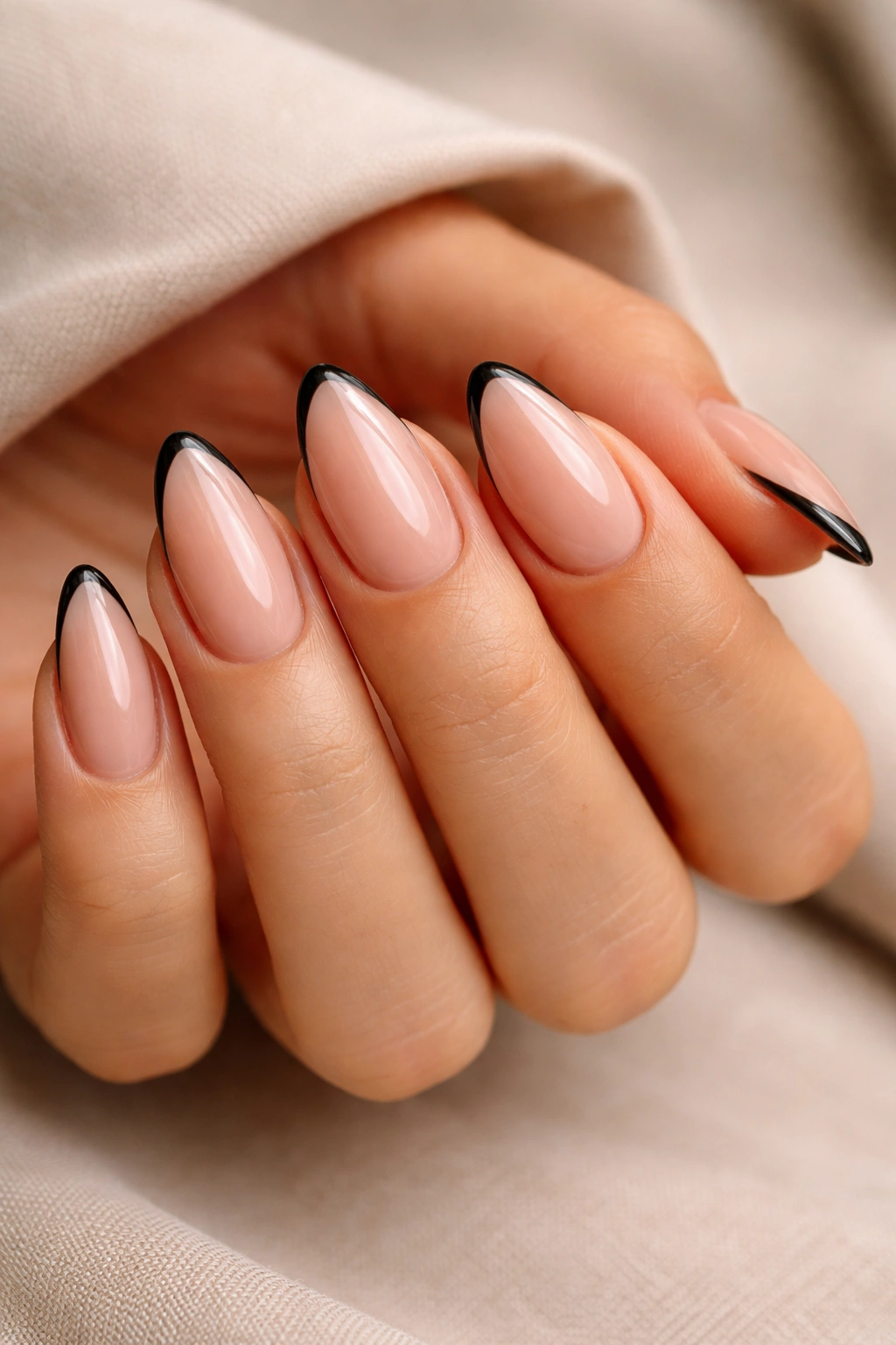 Close-up of an almond nail with a slim black French tip on a sheer nude base, studio lighting.