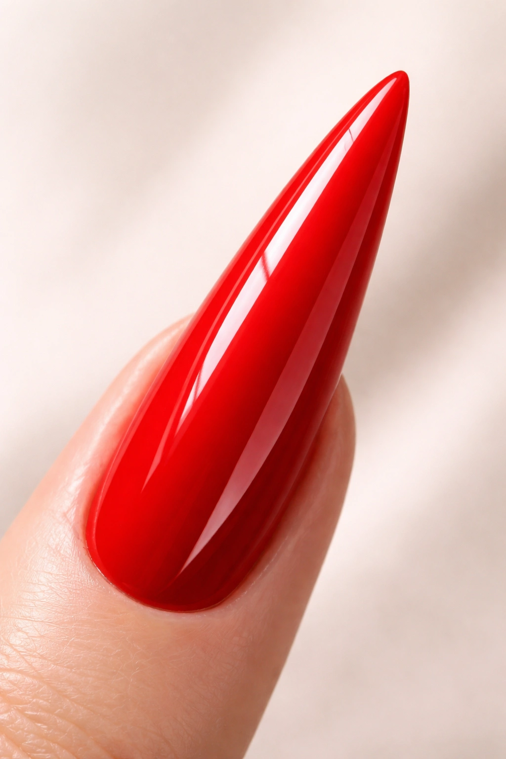 Close-up of a single glossy red stiletto nail on a neutral background