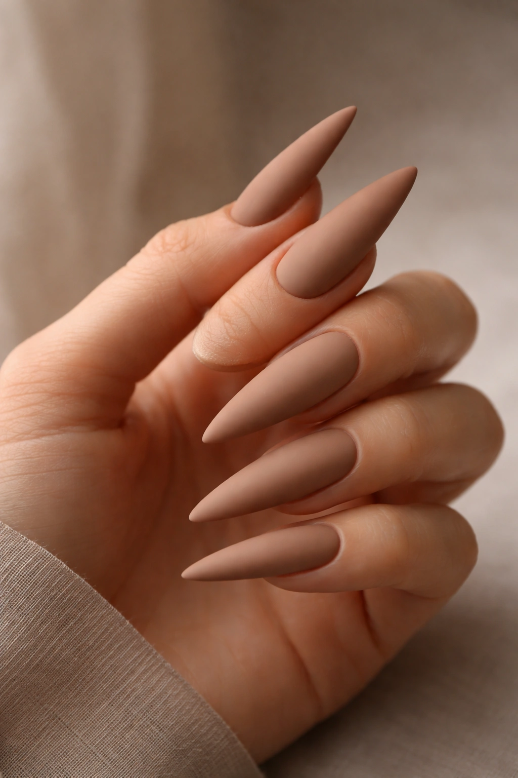 Clay nude matte stiletto nails on neutral background