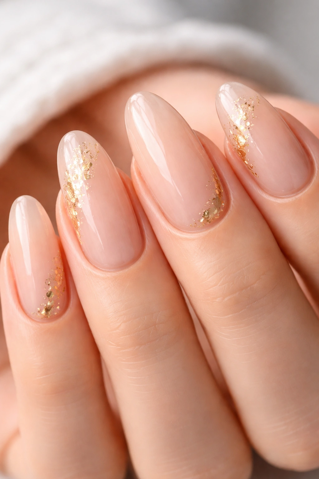 Close-up of long oval nails with clear base and delicate gold foil flecks