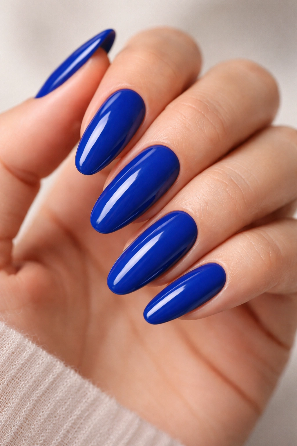 Close-up of long oval nails painted cobalt blue with cream finish on bare hand