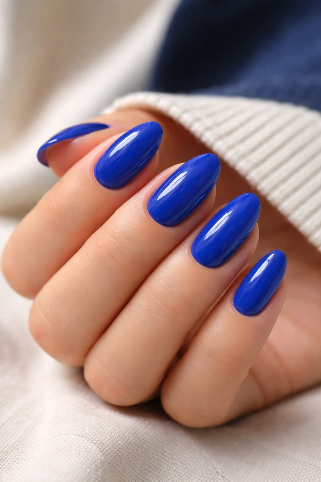Close-up of cobalt blue short almond nails with a sharp clean shape and glossy finish