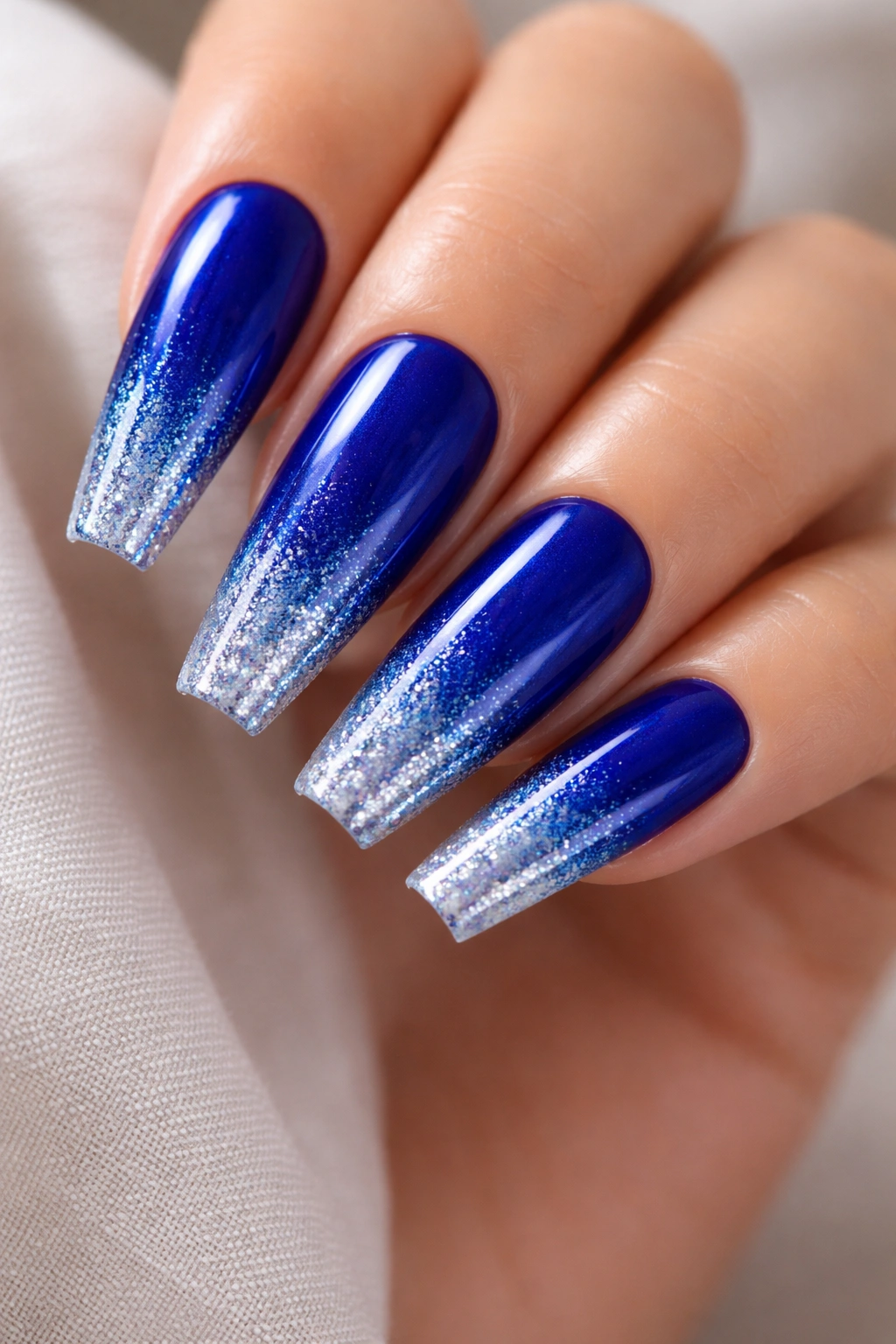 Close-up of cobalt to metallic blue ombre coffin nails with sparkle tip fade in a studio