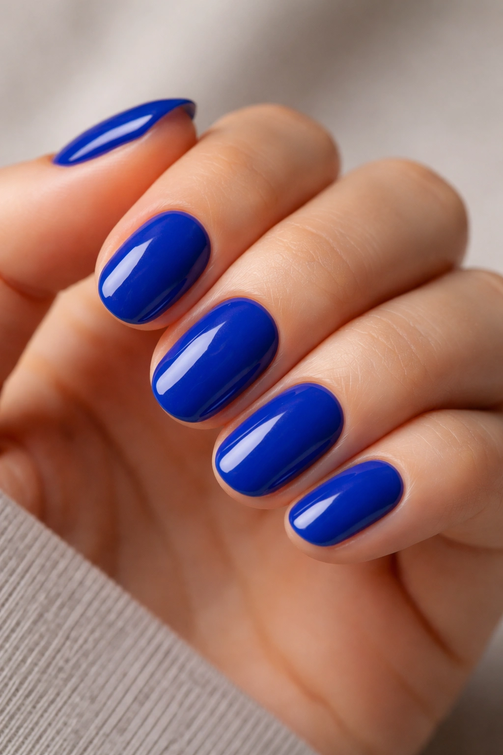 Close-up of short oval nails painted solid creme cobalt blue with a smooth, saturated finish