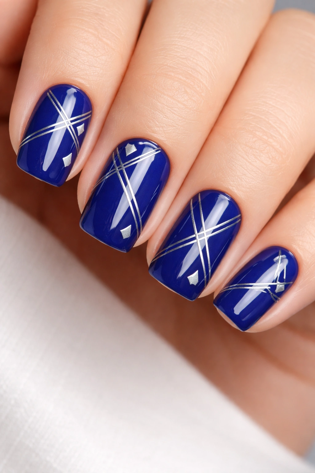 Close-up of cobalt blue short squoval nails with silver geometric patterns