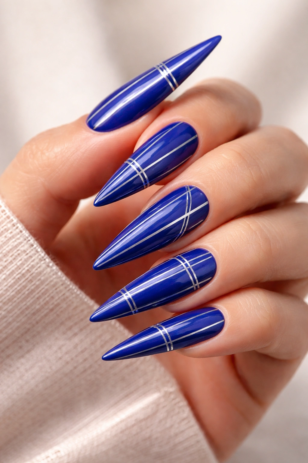 Close-up of cobalt blue stiletto nails with thin silver stripes on a neutral background