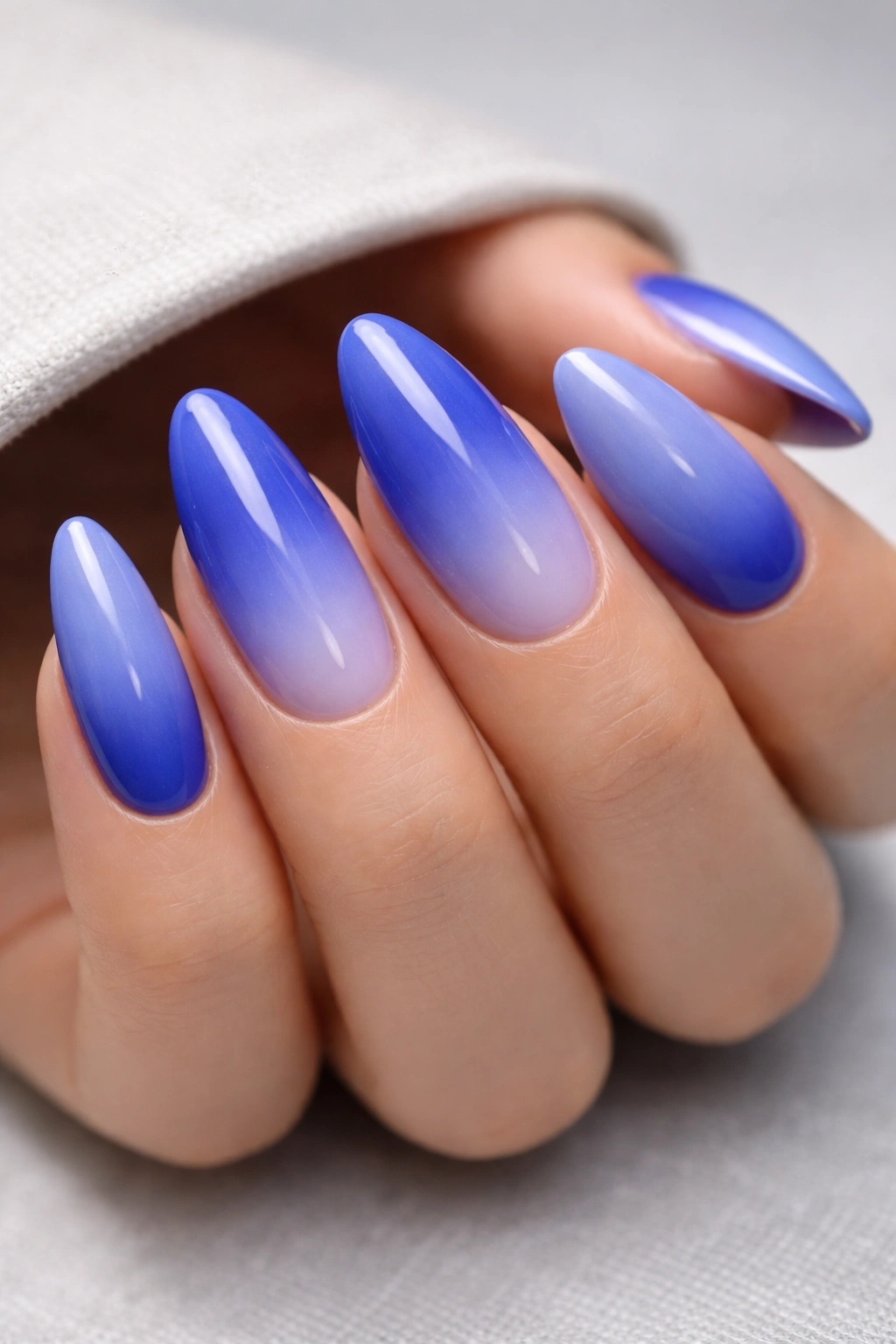Macro close-up of almond nails gradient from cobalt blue to periwinkle with a glossy finish