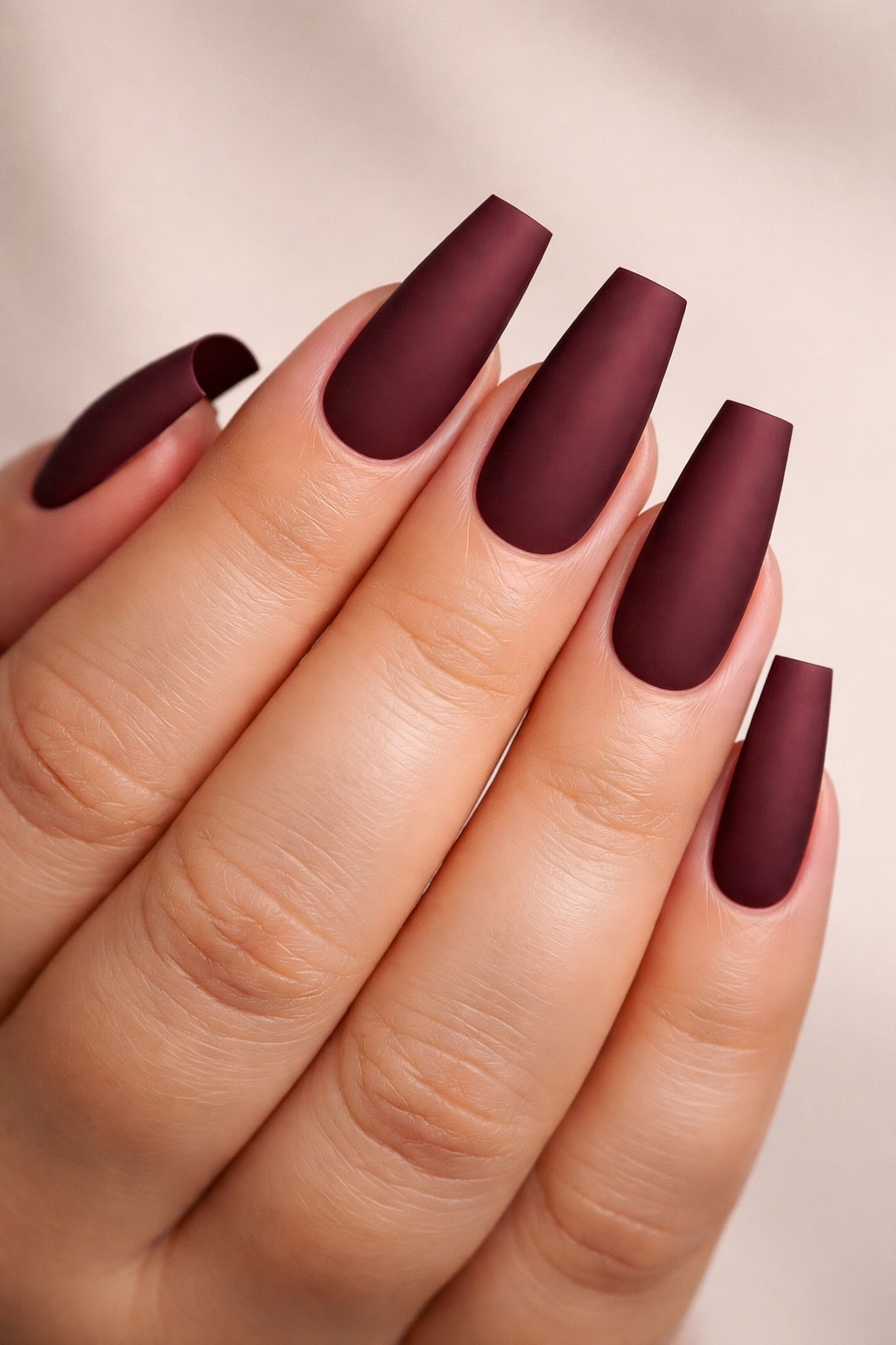 Close-up of coffin nails with squared tips and matte burgundy polish