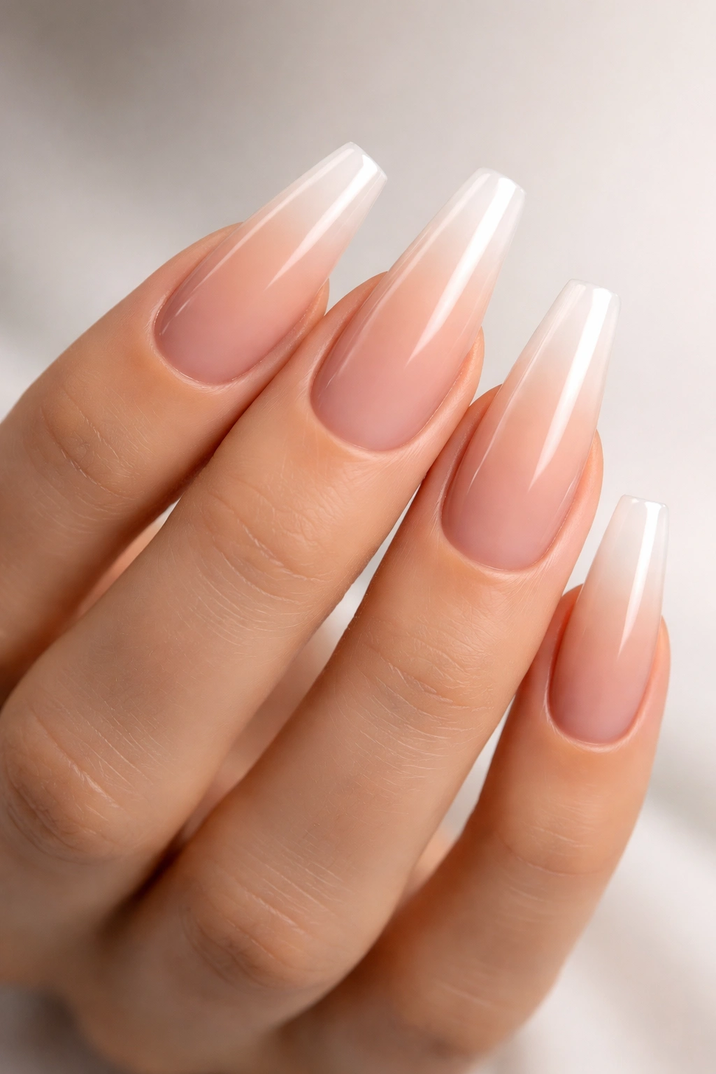 Close-up of coffin-shaped nails with a nude-pink to clear ombré gradient.