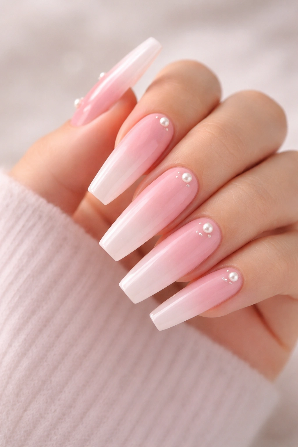 Close-up of coffin nails in soft pink ombré with pearl accents on a neutral backdrop