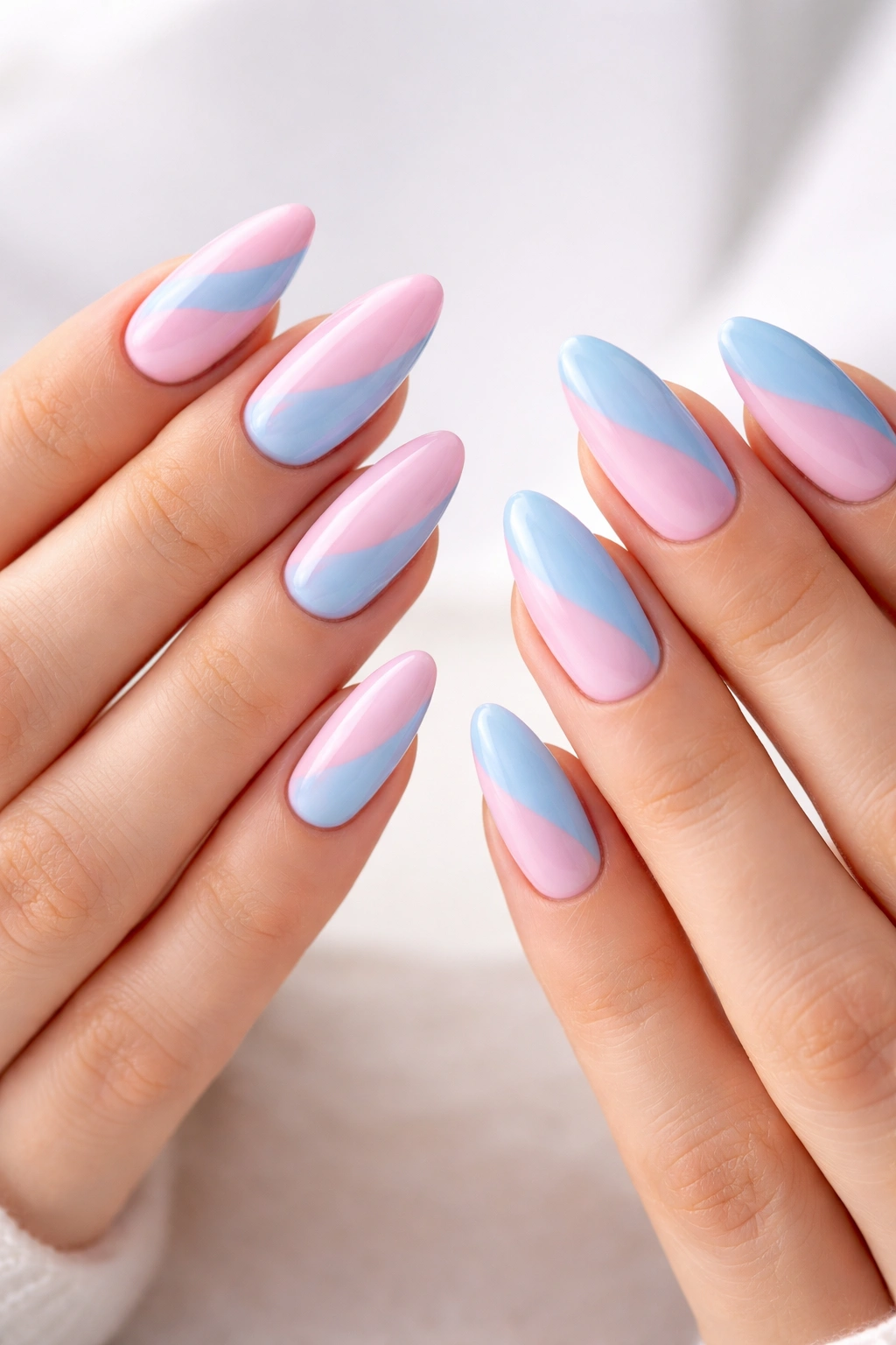 Two hands with almond nails in opposite color-block designs, pink/blue swap
