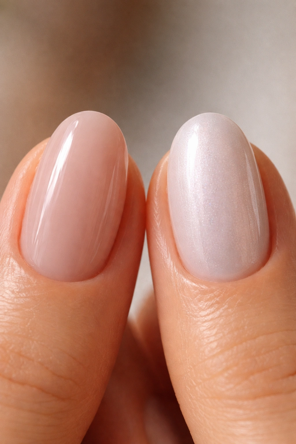 Two short oval nails showing sheer nude and pigmented pearl finishes