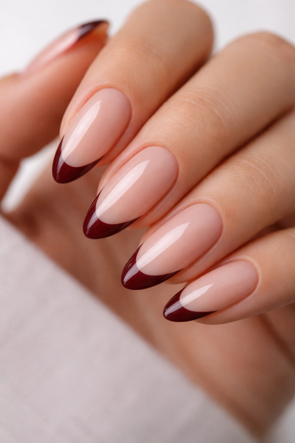 Close-up of almond nails with nude base and burgundy tips