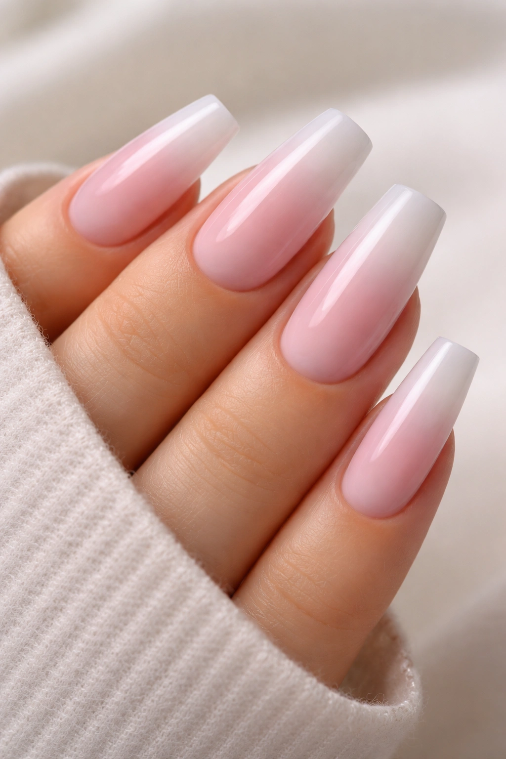 Close-up of medium coffin nails with cool pink to white ombre gradient on a bare hand