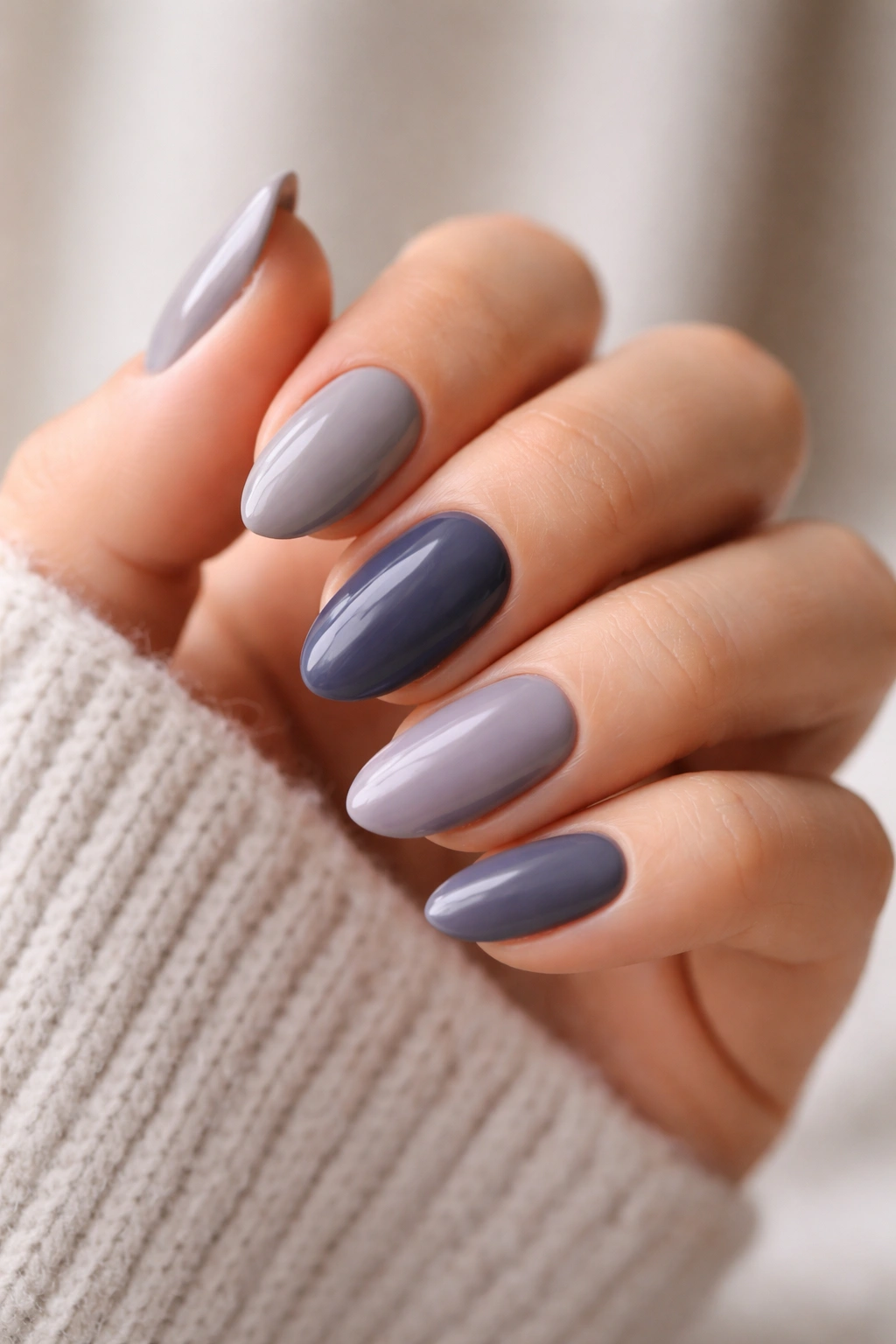 Hand with several cool-tone almond nails in gray-beige, navy, and dusty lilac.