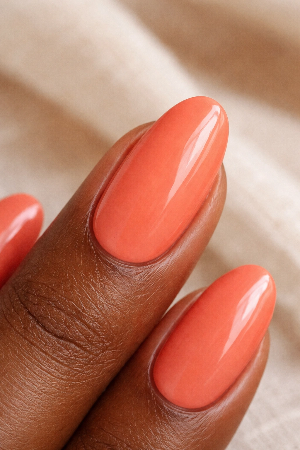 Close-up of a fingernail painted coral with warm undertones