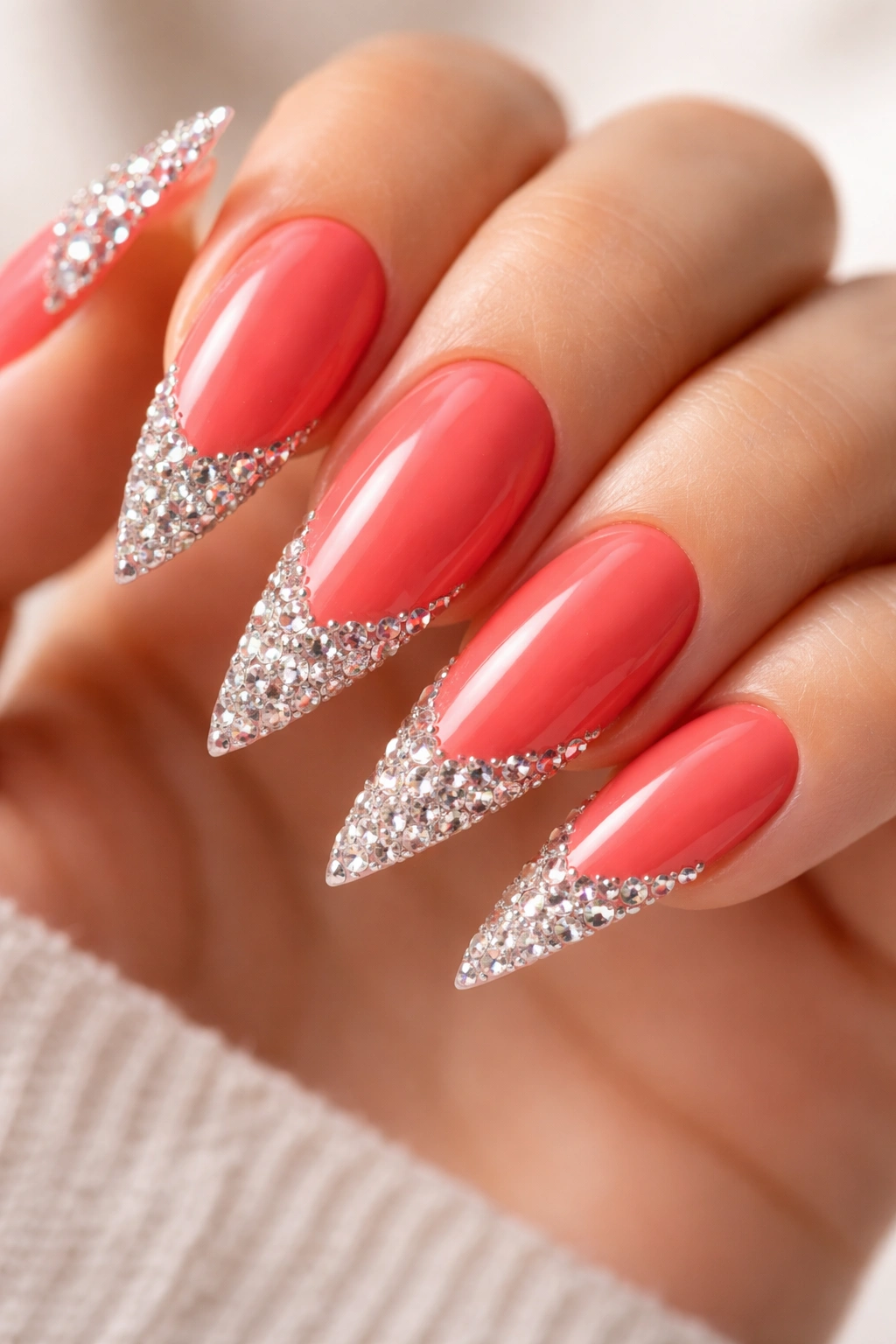 Close-up of coral stiletto nails with rhinestone tips.