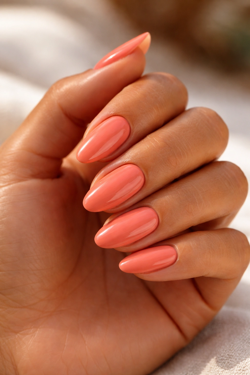 Close-up of hand with warm coral nails on tan skin under soft light
