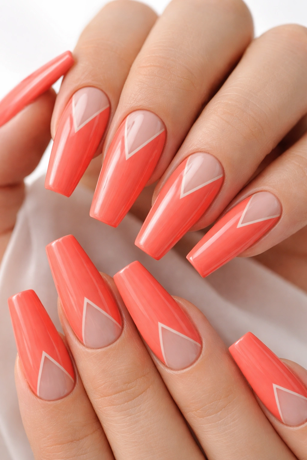 Close-up of bright coral coffin nails with negative-space triangles on a white background