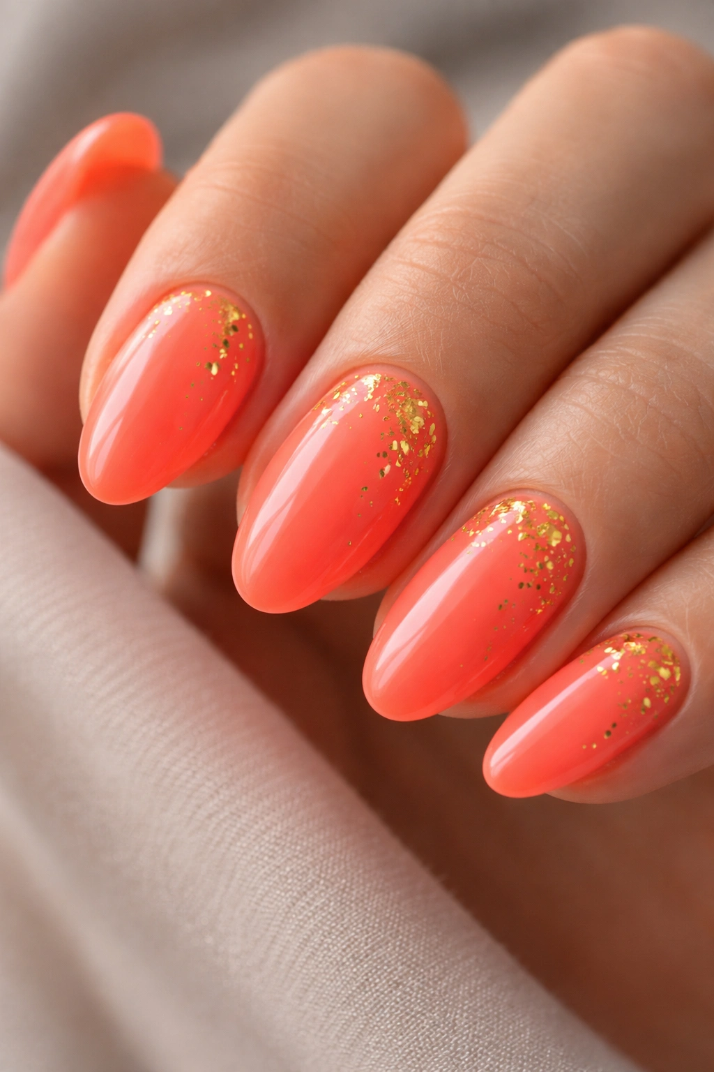 Close-up of coral-neon short almond nails with gold foil flakes