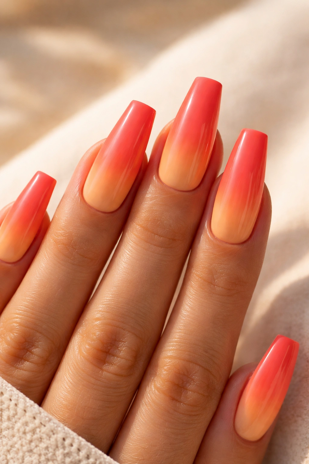 Close-up of coral to peachy orange ombre nails on medium coffin shape