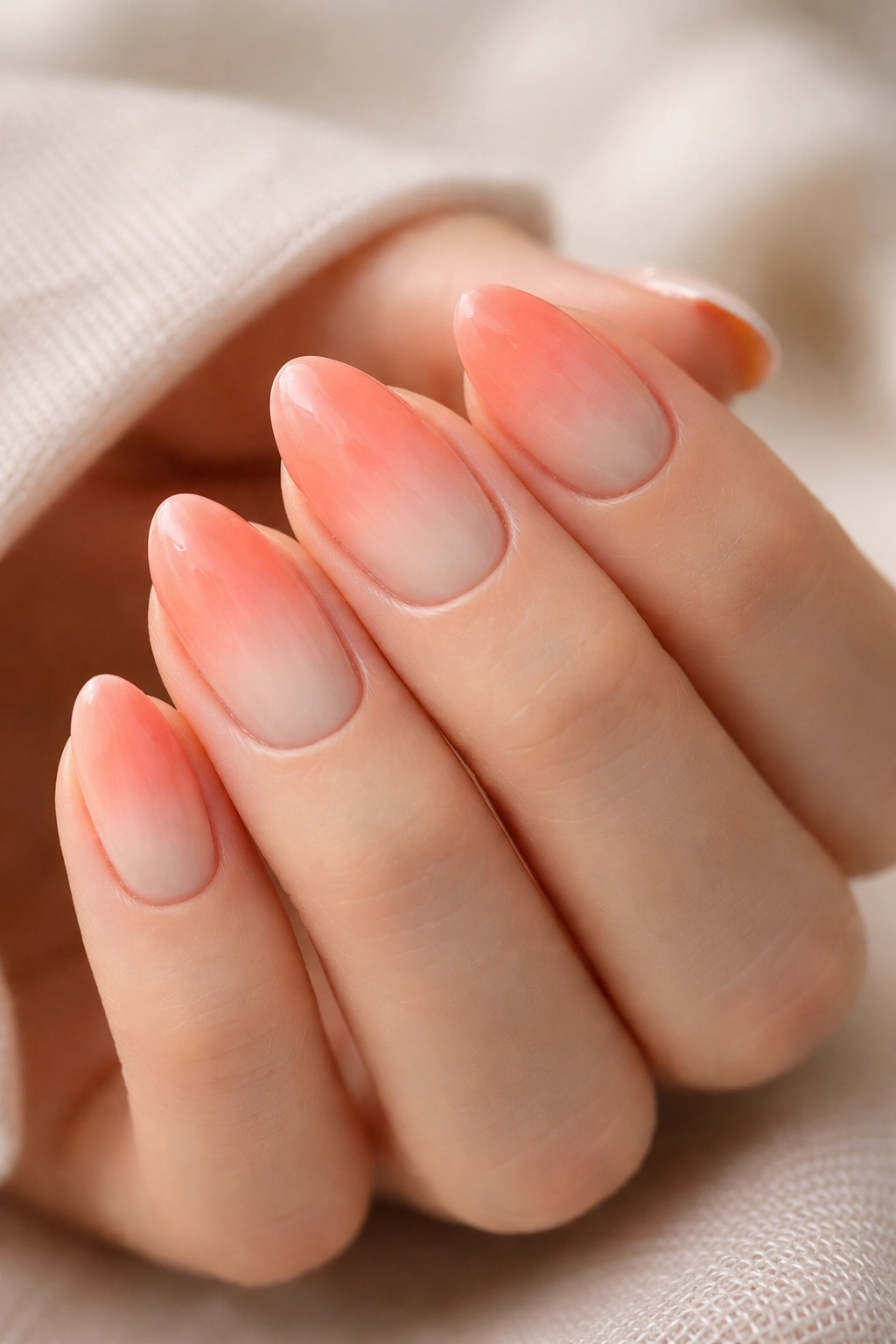 Close-up of short almond nails with coral ombre fading into cream at the tip