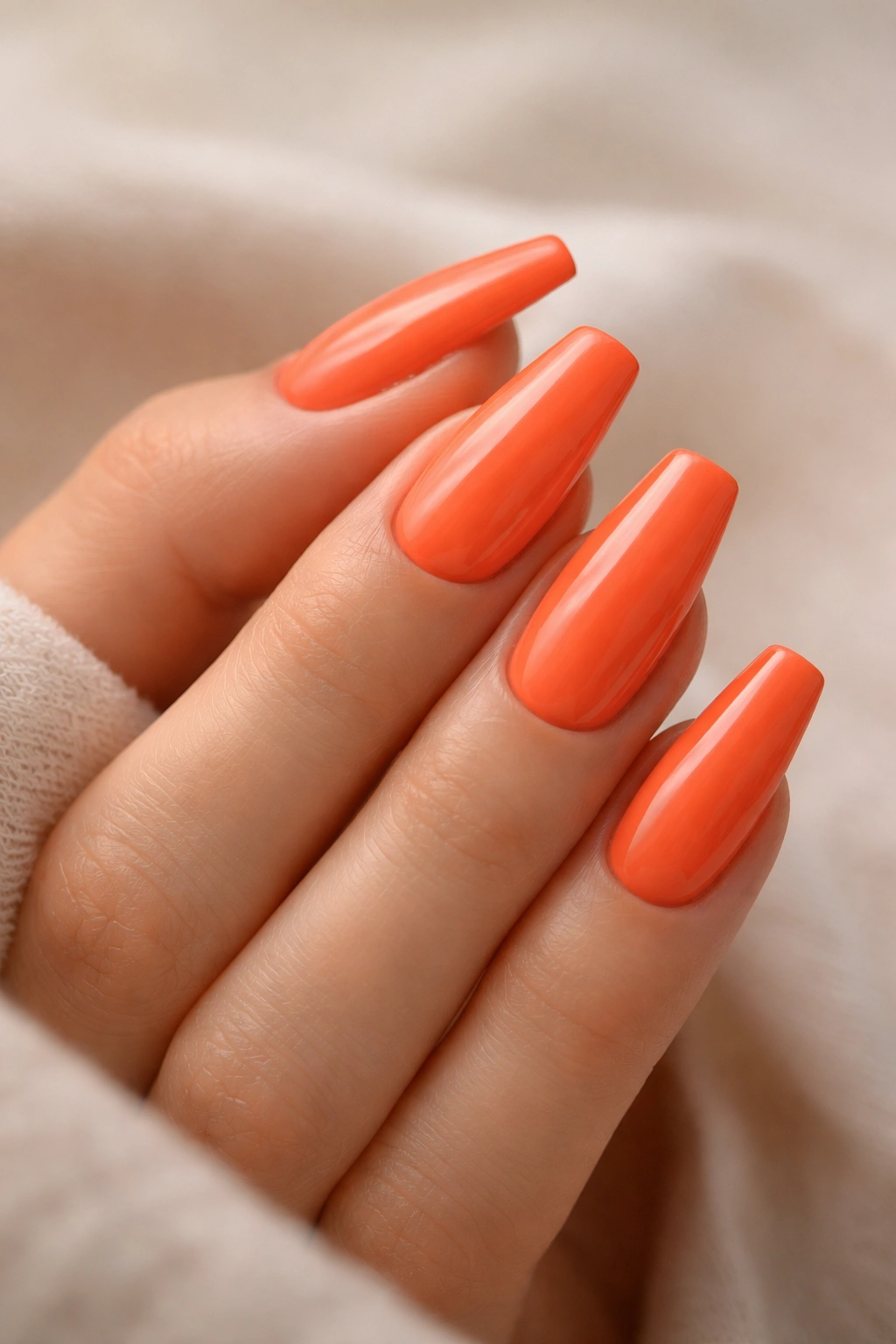 Close-up of a hand with medium coffin nails in vibrant coral orange
