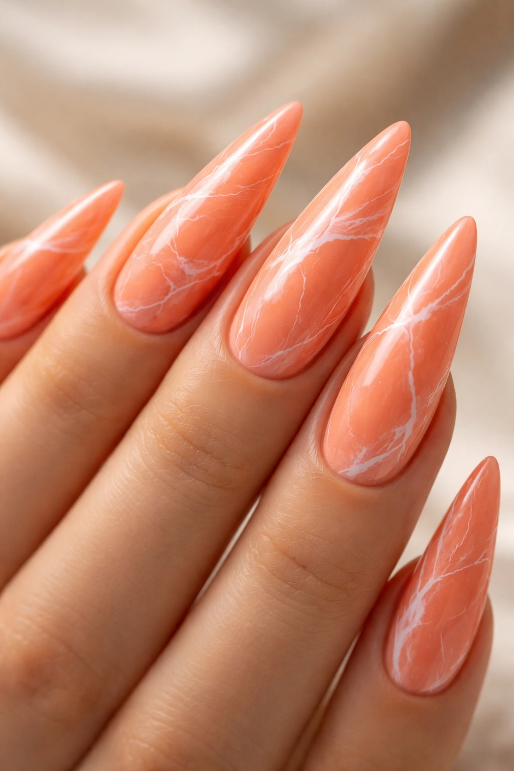 Close-up of coral orange stiletto nails with white marble veining