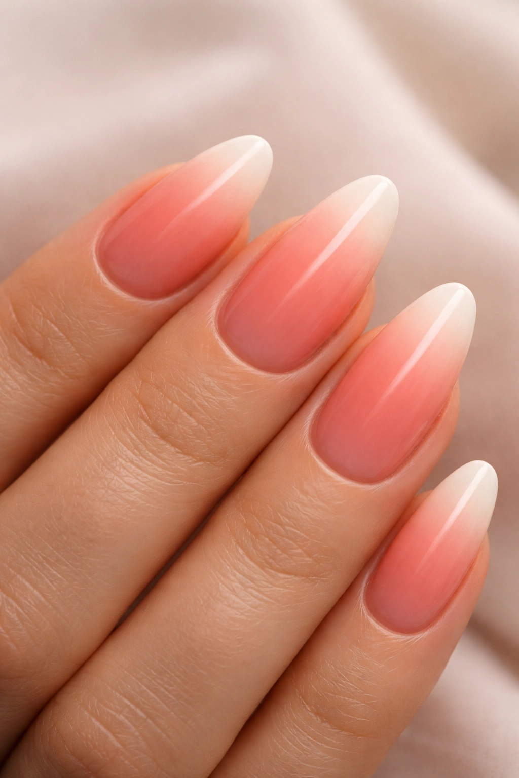 Almond nails with coral pink to ivory gradient in warm lighting