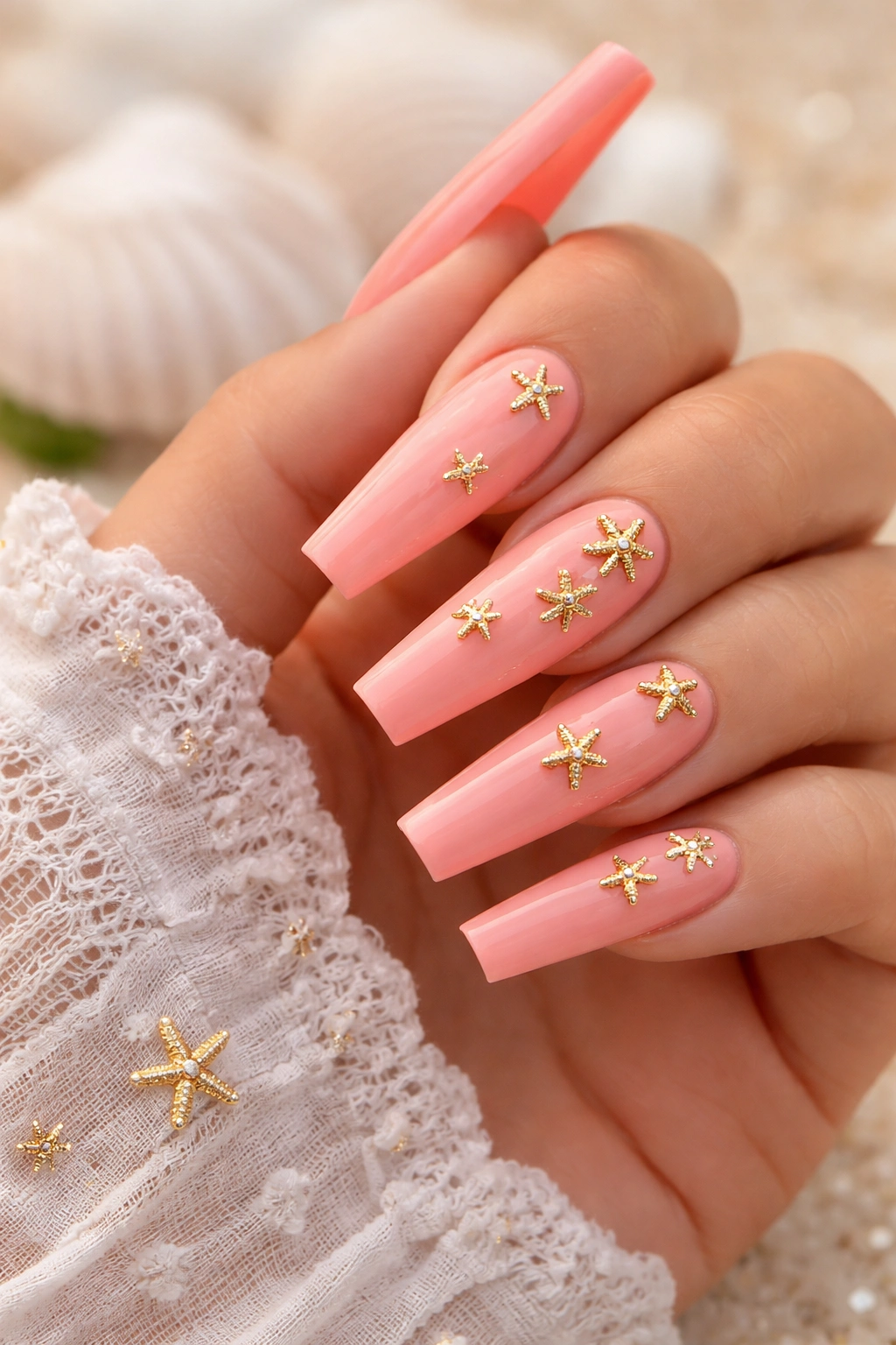 Coral pink nails with small gold starfish charms scattered across nails