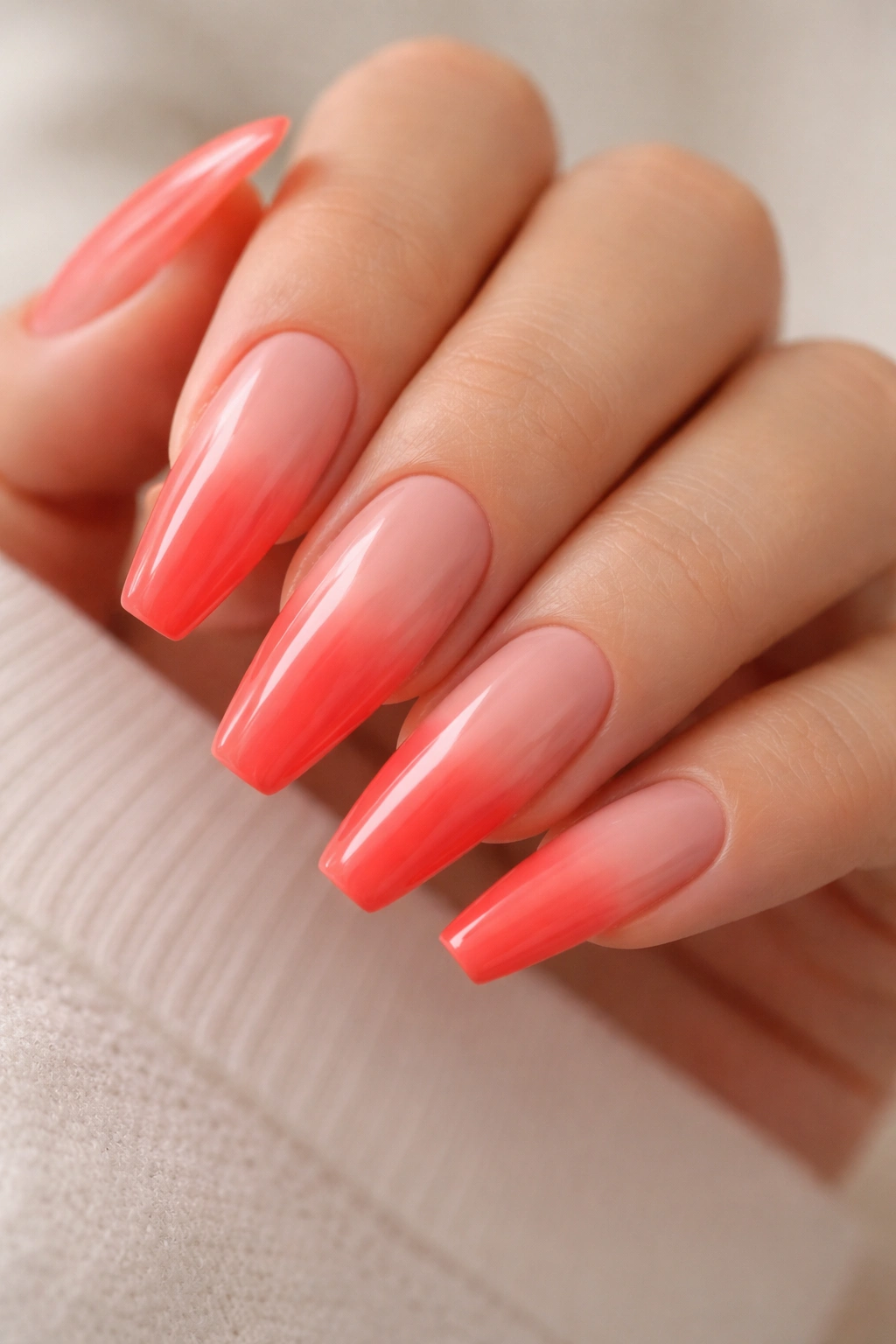 Close-up of coral-red fade nails on long ballerina tips with nude base near cuticle