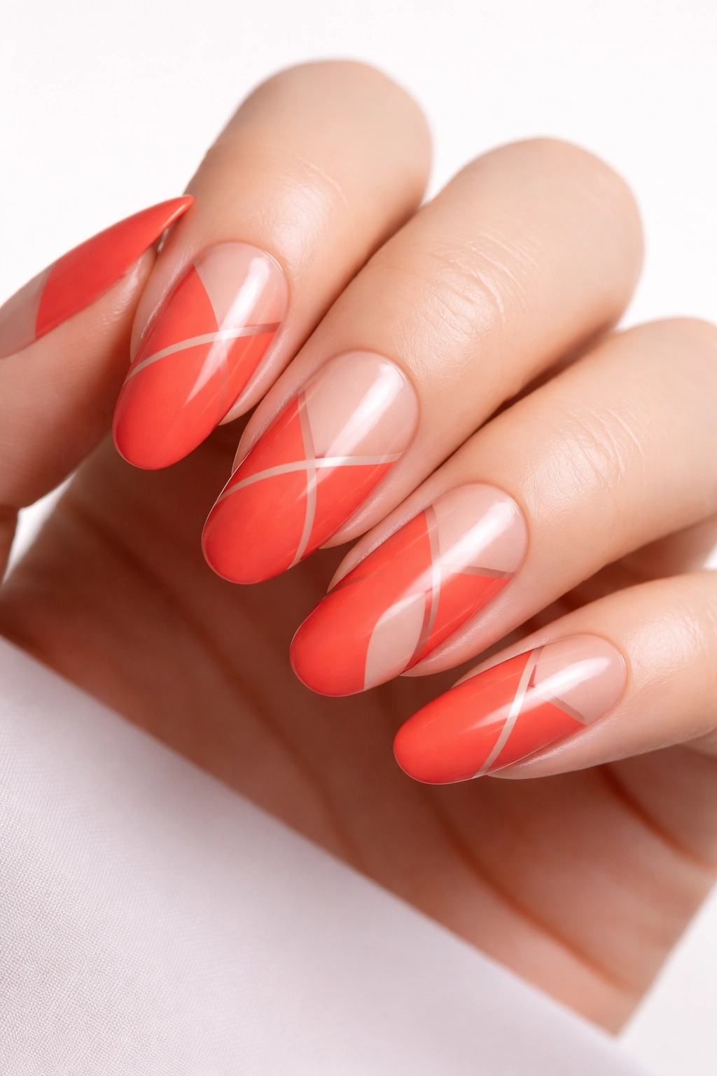 Close-up of coral-red long rounded nails with negative-space geometric patterns on a neutral background.
